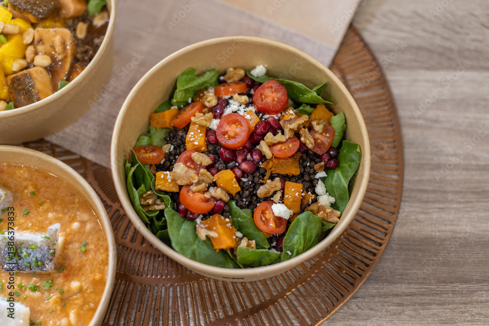 A healthy salad with black lentils, spinach, cherry tomatoes, walnuts, pomegranate, pumpkin, and feta. Horizontal close-up on a wooden surface. Healthy grab-and-go concept, biodegradable packaging A healthy salad with black lentils, spinach, cherry tomatoes, walnuts, pomegranate, pumpkin, and feta. Horizontal close-up on a wooden surface. Healthy grab-and-go concept, biodegradable packaging