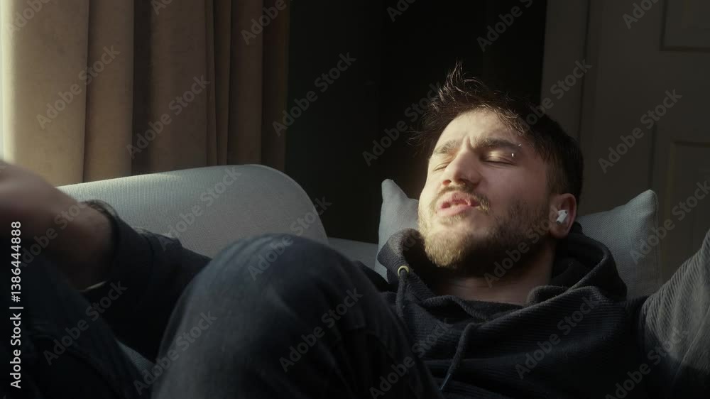 Young Man Enjoying Music and Dancing Playfully on a Couch in Sunlight Young Man Enjoying Music and Dancing Playfully on a Couch in Sunlight