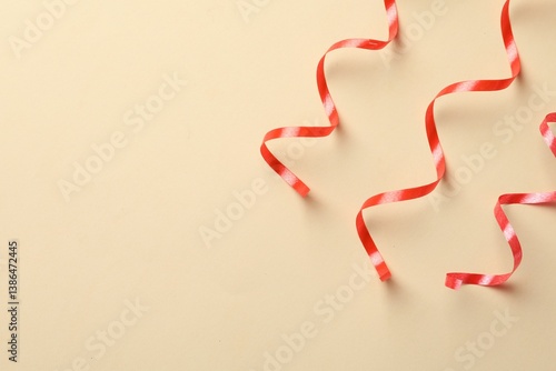 Shiny red serpentine streamers on beige background, flat lay. Space for text