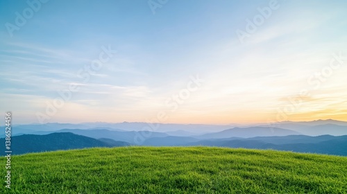 A vibrant green hill dominates the foreground, gently sloping towards a distant mountain range. The sky is a serene blend of blue and soft pastel hues at sunset. The image is high-resolution, showca