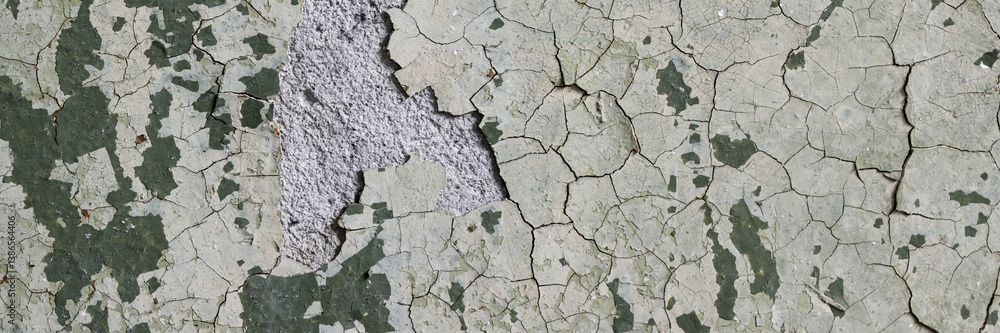 Peeling paint on the wall. Panorama of a concrete wall with old cracked flaking paint. Weathered rough painted surface with patterns of cracks and peeling. Grunge texture for wide panoramic background