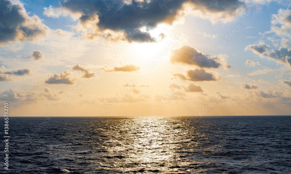 Obraz premium Beautiful golden sunset with a hint of blue sky over calm ocean, sun hiding behind a cloudscape, reflection of sunbeams on water. Eternal, peaceful mood.
