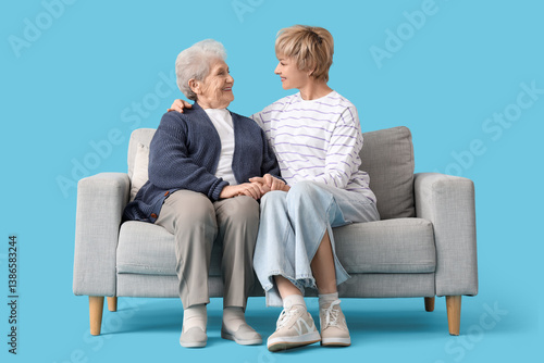 Mature woman with her mother sitting on sofa against blue background