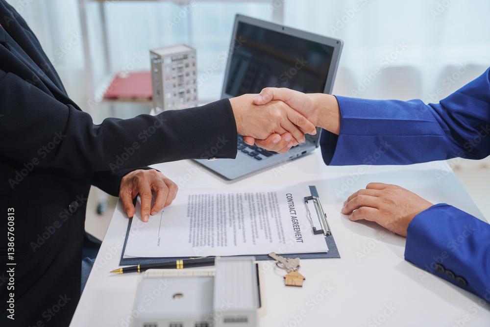 Two people shaking hands over a desk with house model and keys, symbolizing a real estate deal, contract signing, or successful negotiation. Bright office setting emphasizes professionalis Two people shaking hands over a desk with house model and keys, symbolizing a real estate deal, contract signing, or successful negotiation. Bright office setting emphasizes professionalis