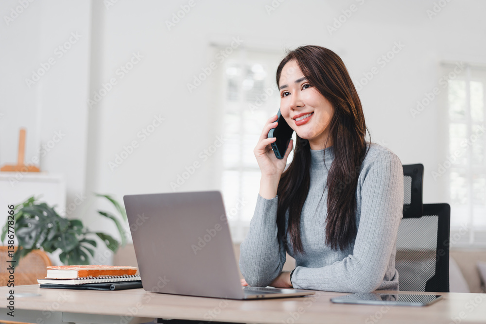 Cheerful woman working on laptop while talking on phone in bright home office setting. Cheerful woman working on laptop while talking on phone in bright home office setting.