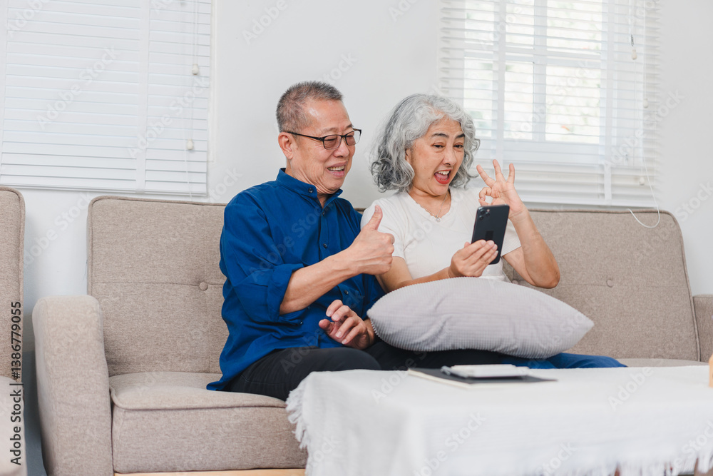 Obraz premium Elderly couple sitting on sofa, smiling and making gestures while video calling on smartphone, enjoying cheerful moment.
