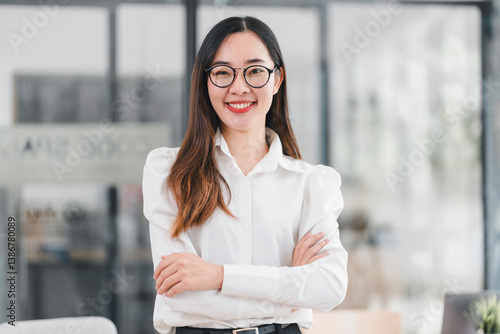Cuadro en lienzo Confident young woman in white shirt and glasses standing with arms crossed in modern office setting