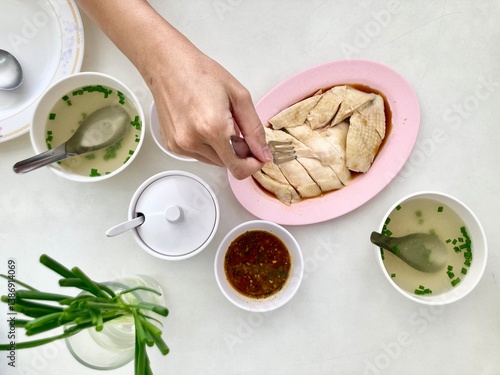 a woman is scooping a plate of cut Betong chicken with a special sauce and green onions as a side dish and a rich chicken bone soup on the white table