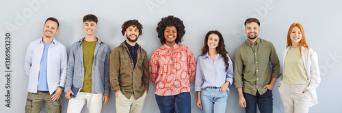 Banner with a group portrait of happy diverse people posing by a gray wall. Team of smiling Caucasian and African American men and women in casual clothes standing on a gray color background