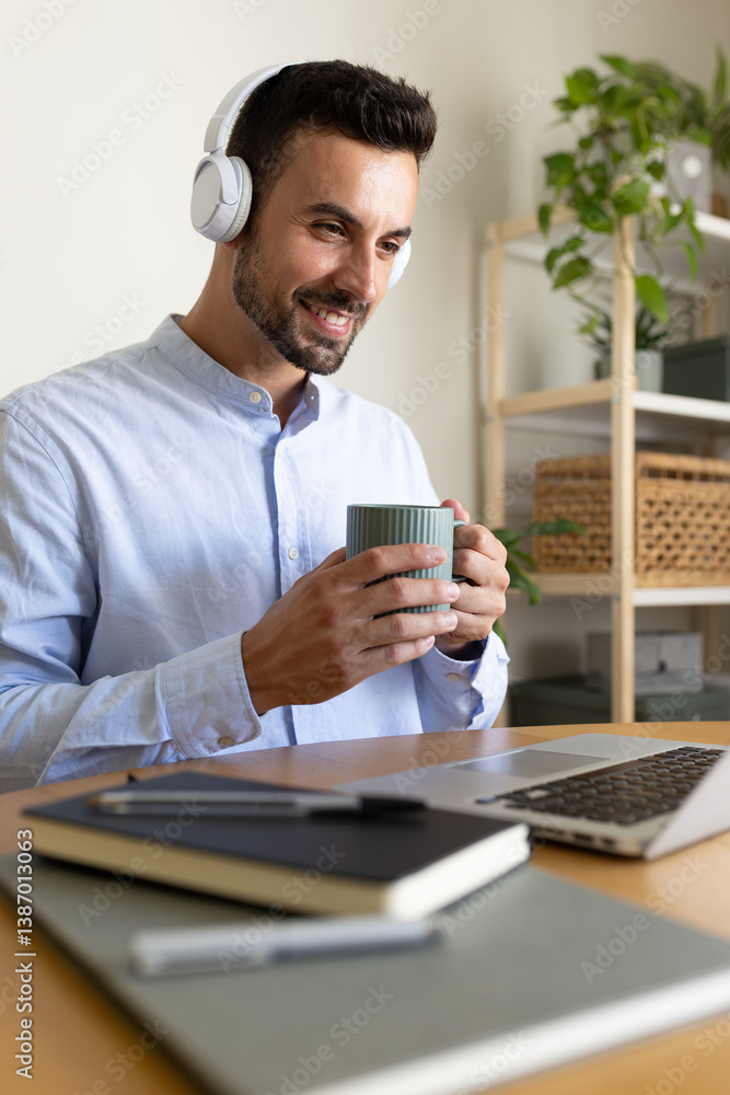 Vertical portrait of relaxed man with headphones drinking coffee while working at home office using laptop. Vertical portrait of relaxed man with headphones drinking coffee while working at home office using laptop.