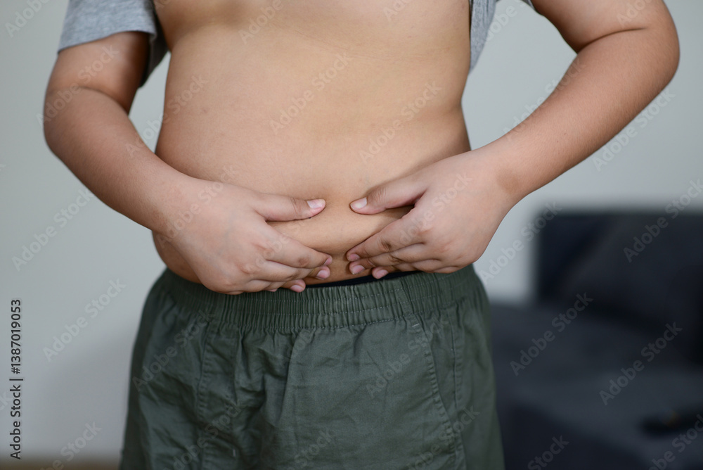 A fat child with a fat belly holds his stomach with his hands.