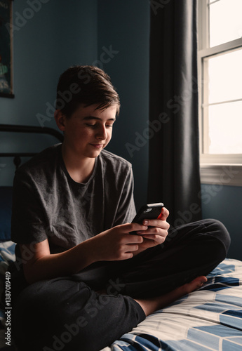 Close up of teen boy in bedroom using smartphone on his bed.