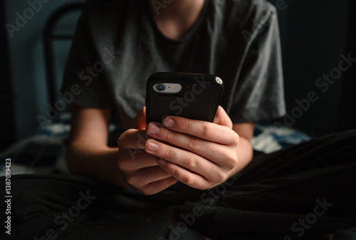 Close up of hands of teen boy holding smartphone sitting on bed.