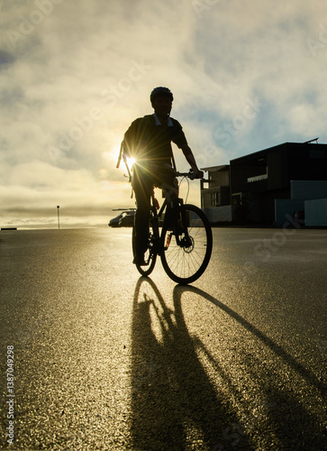 Obraz na płótnie Cyclist in silhouette riding on the suburb road at sunrise. Sun starburst shining from behind. Auckland. w salonie