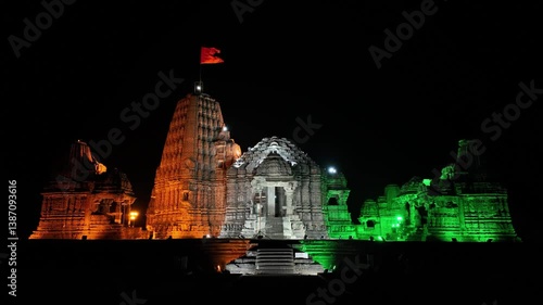 aerial night view of Gondeshwar Hindu temple of India illuminated in the colors of Indian flag: orange, white, green. saffron flag flies atop. stonework of temple is highlighted by strategic lighting