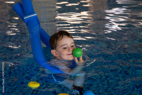 Toddler learning to swim and playing with ball in indoor pool