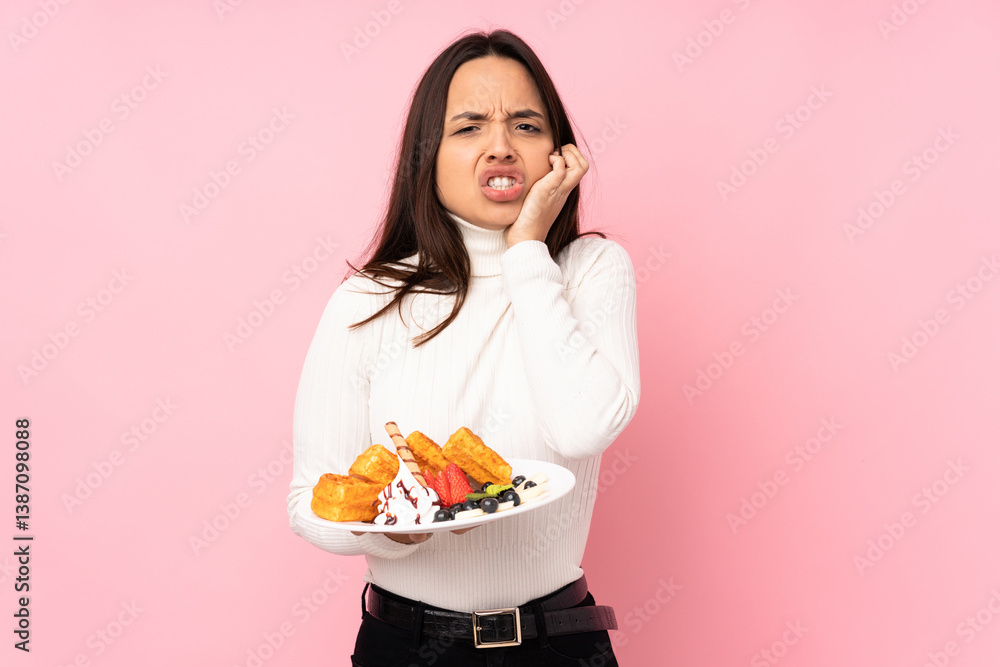 Young brunette woman holding waffles over isolated pink background with toothache Young brunette woman holding waffles over isolated pink background with toothache