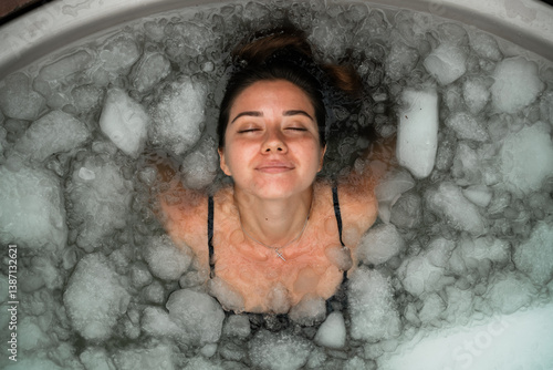 Woman practices cold therapy in an outdoor ice bath surrounded by tropical plants. A peaceful moment of self-care and healing