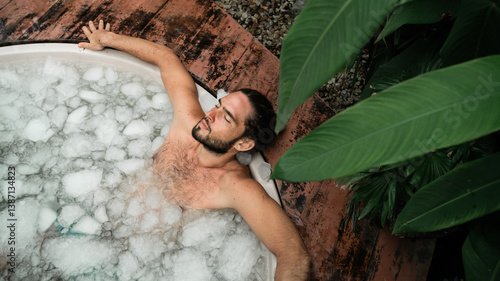 Man takes an ice bath outdoors in a lush tropical setting. Cold immersion for mental strength, discipline, and physical recovery