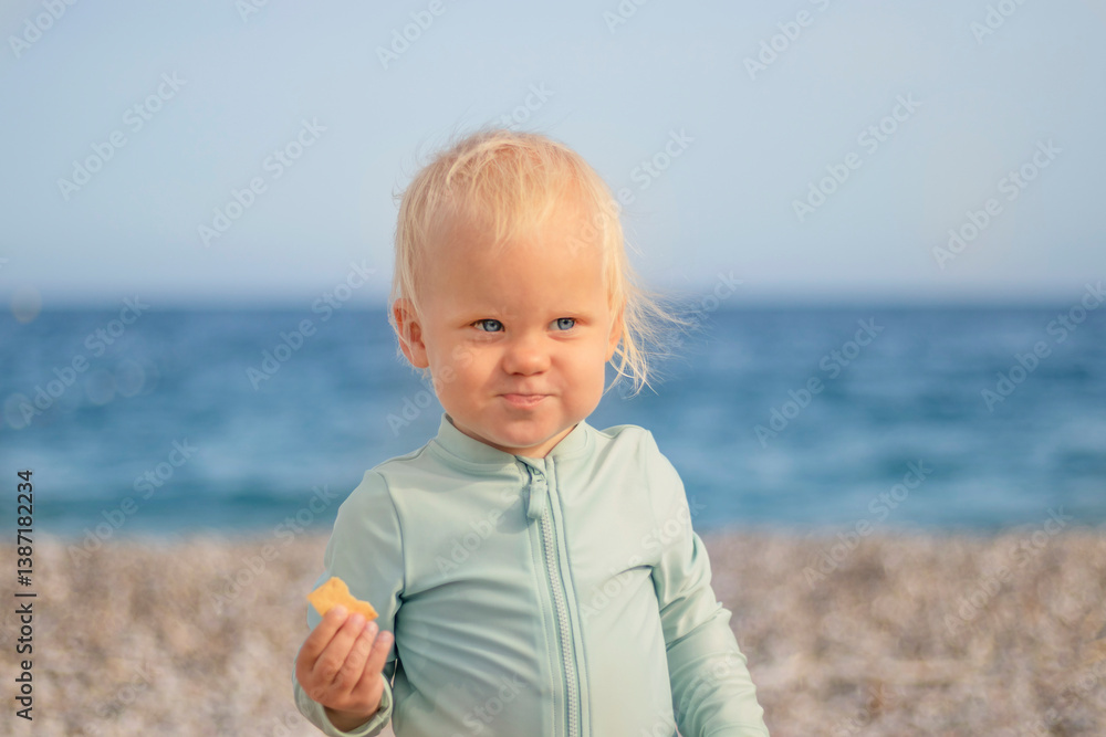 A joyful toddler contentedly enjoying a delightful snack by the beach, with sea waves splashing in the background