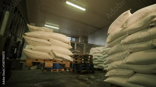 Large stacks of white sugar bags stored in a warehouse, organized on pallets under artificial lighting in an industrial storage facility.