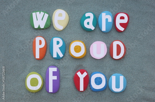 We are proud of you, motivational slogan and message composed with multi colored hand painted stone letters over green sand
