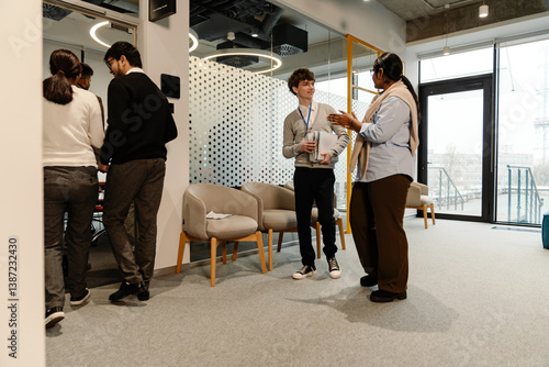 Εκτύπωση καμβά In an office, a multiethnic group of formally dressed people is entering a meeting room, with a White man in his 20s, holding documents and talking to an Indian woman in her late 20s who gestures