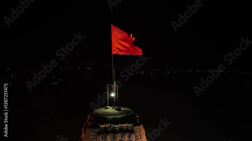 illuminated orange flag on ancient Hindu temple. waving prominently against a calm night sky. The aerial drone video captures a profound sense of historical importance and cultural pride.