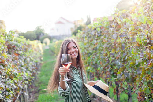 Woman with wineglass of pink wine in vineyard. Wine tasting in winery. Traveler on vacation. Happy celebration, tour on vine plantation. Authentic farm lifestyle. Farmer enjoying harvest
