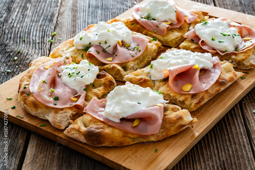 Pinsa Romana with mortadella, burrata cheese and pistachio on wooden table	