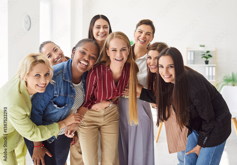 Group portrait of happy diverse women standing together in office and hugging each other. Happy female colleagues or friends laughing and embracing, showing unity and teamwork in positive atmosphere.