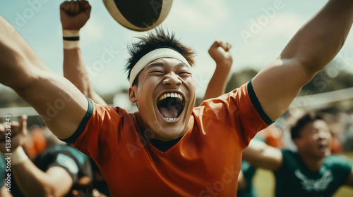 A jubilant Asian athlete celebrates a victorious moment during a rugby match, surrounded by cheering teammates.