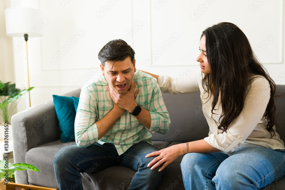 Man having breathing problems and choking while sitting on sofa and his wife helping him at home