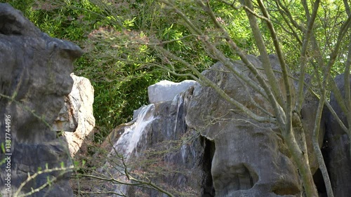 A waterfall is flowing down a rocky hill. The rocks are grey and the water is clear. There is a tree in the background