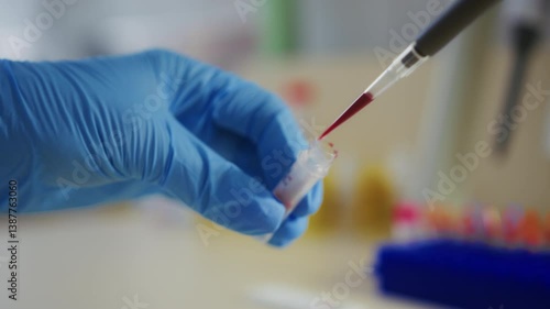 A scientist in blue gloves carefully pours blood into a test tube
