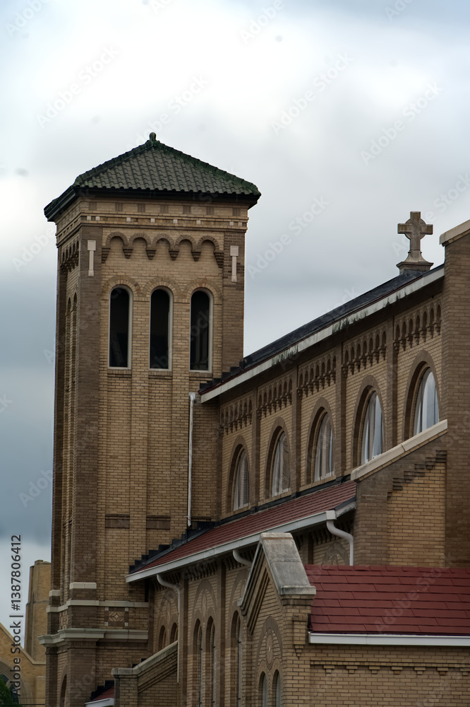 Obraz premium Historic Brick Church with Tower and Cross Against Cloudy Sky