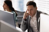 Focused company employee man working at computer monitor in office with colleagues, looking at display, thinking hard on job task, touching head, temple, reading or watching content