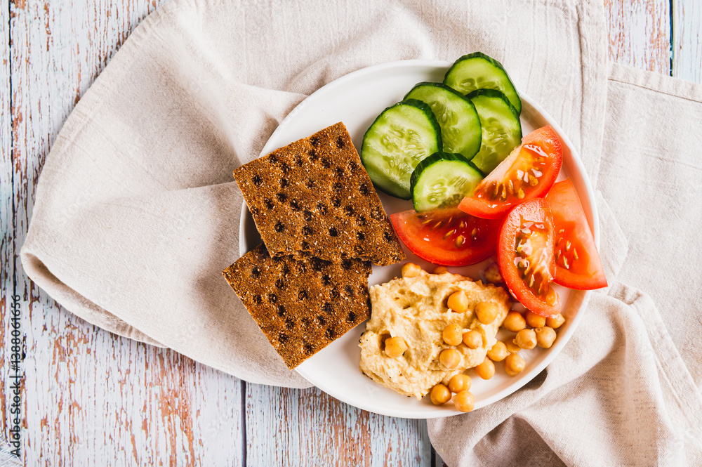 Close up of platte with hummus, chickpeas, tomato, cucumber and grain crackers on a plate top view