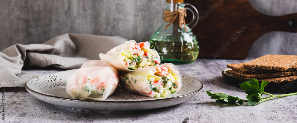 Spring rolls in rice paper with crab sticks, cucumber, greens and sauce on a plate on web banner