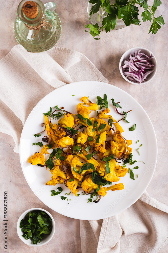 Baked spicy cauliflower with onions and parsley on a plate on the table top and vertical view