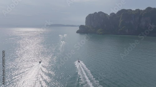 longboats sailing the sea near limestone cliffs at Railay beach in Krabi, Thailand.