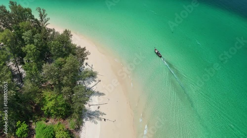 Top view of wooden longtail boat sailing in transparent turquoise sea waters near shoreline of tropical island in Andaman Sea, Thailand