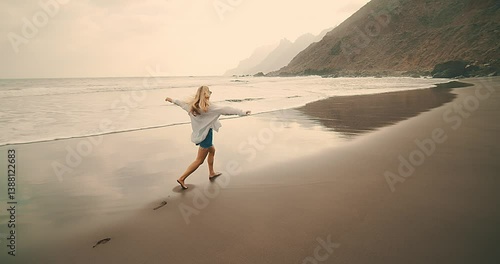 Woman Walking Alone by the Ocean. She strolls peacefully along the shoreline, embraced by the sound of waves and the fresh sea breeze. Solitude, mindfulness, connection with nature.