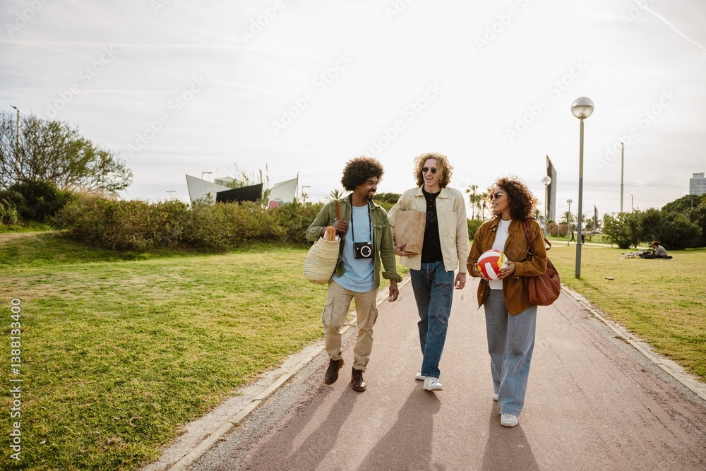 Group of three friends walking and talking while laughing and holding a bag, package, and ball, outdoors, on a walk Group of three friends walking and talking while laughing and holding a bag, package, and ball, outdoors, on a walk