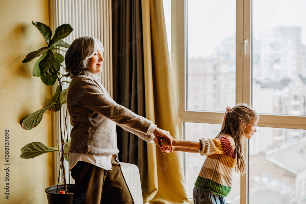 Φωτογραφία Grandmother stands and holds her granddaughter's hands from behind, who stands i