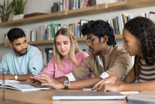 Group study and informal leadership. Smart teenage guy sit at desk in library speak to diverse multicultural classmates students read passage from book propose idea to discuss guide team with insight