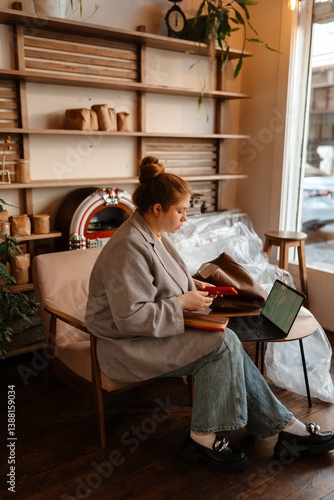 Tablou pe pânză The female owner is holding the phone and sitting near the laptop on the table,