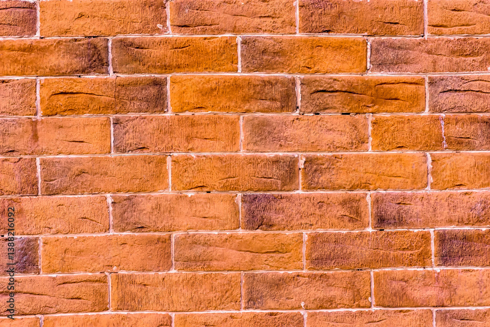 Obraz premium Ściana z dekoracyjnych pomarańczowych cegieł z białymi spoinami zaprawy. Pomarańczowe cegły o szorstkiej fakturze ułożone są w poziomych rzędach, połączone białymi liniami zaprawy. 