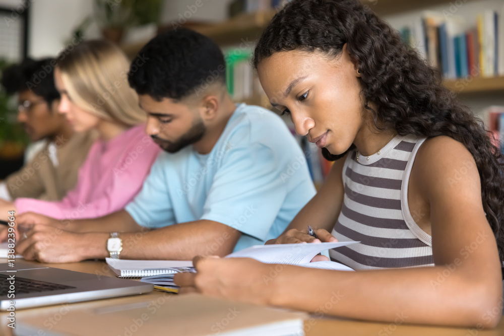 Self training. Busy teen female high school student engaged in studying at library with group of diverse multicultural peers use paper workbooks notebook to search information prepare for lesson exam Self training. Busy teen female high school student engaged in studying at library with group of diverse multicultural peers use paper workbooks notebook to search information prepare for lesson exam