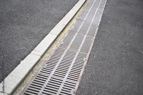 Metal drainage grate along a curb on asphalt road. Urban infrastructure and water drainage system concept.